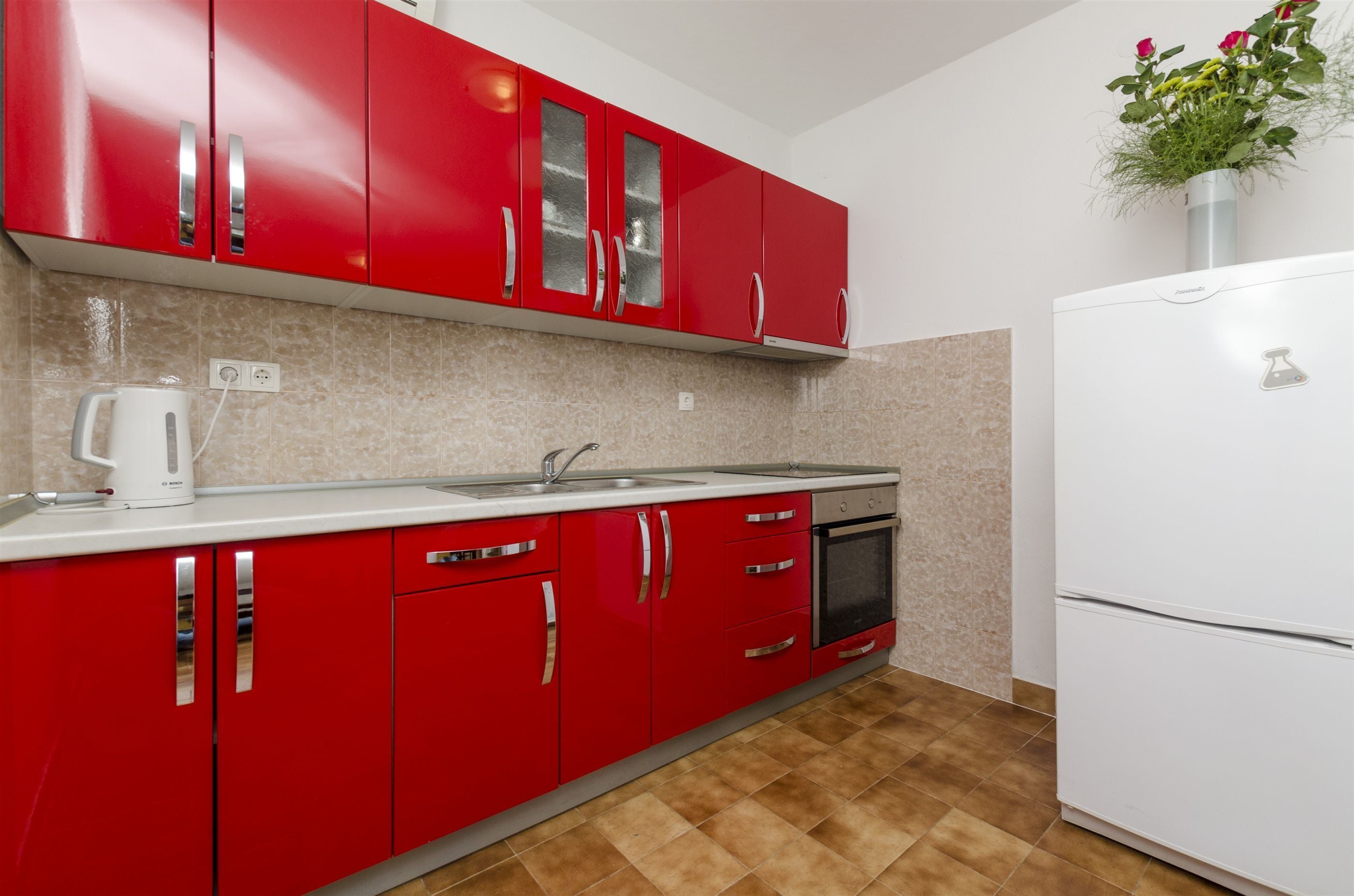 A kitchen with red cabinets, a white countertop, a built-in oven, and a white refrigerator.