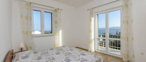 Ein Schlafzimmer mit einem Bett, zwei Fenstern und einem Balkon.