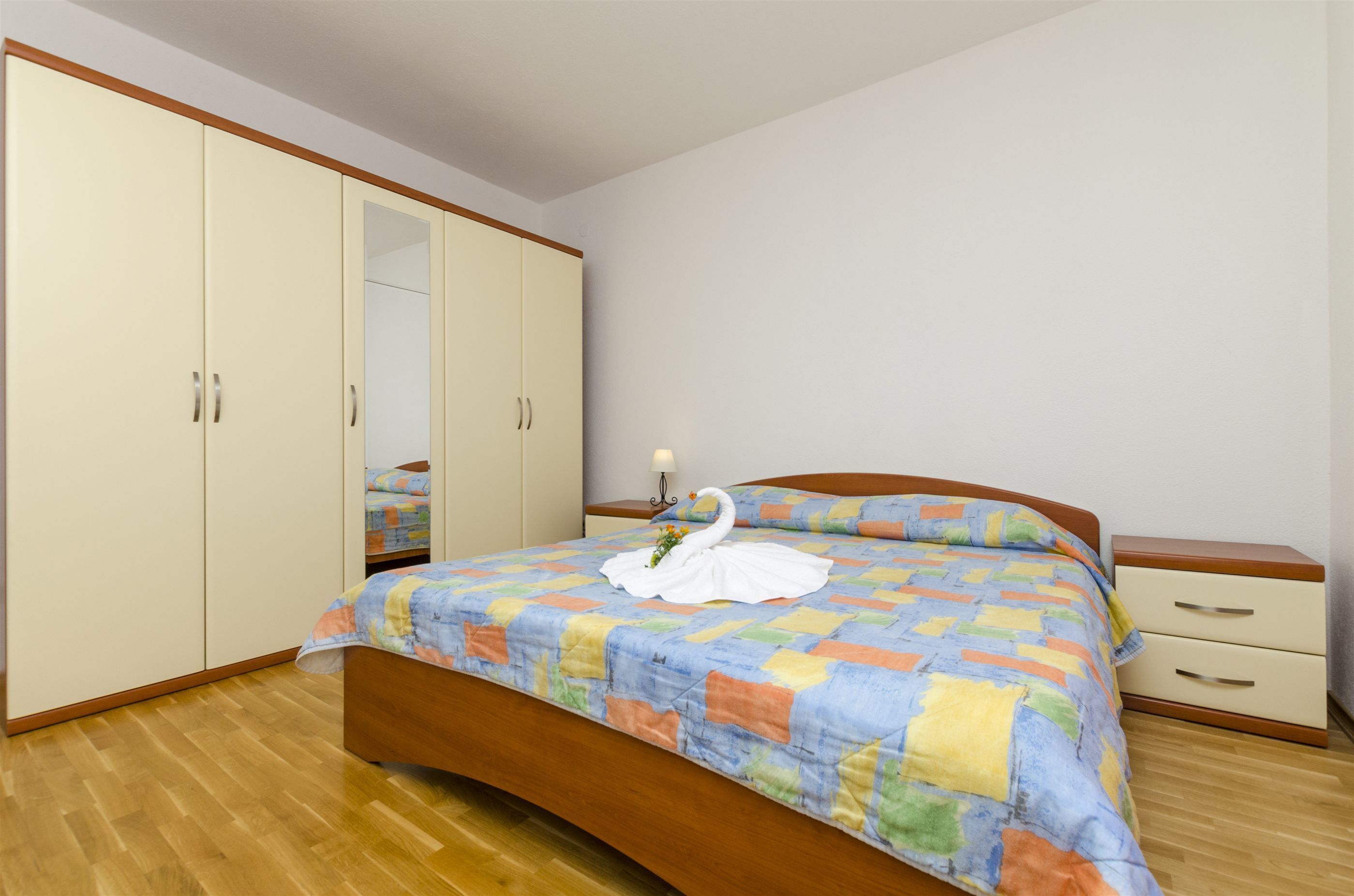 Un dormitorio con cama de madera, colcha colorida, mesita de noche y armario.