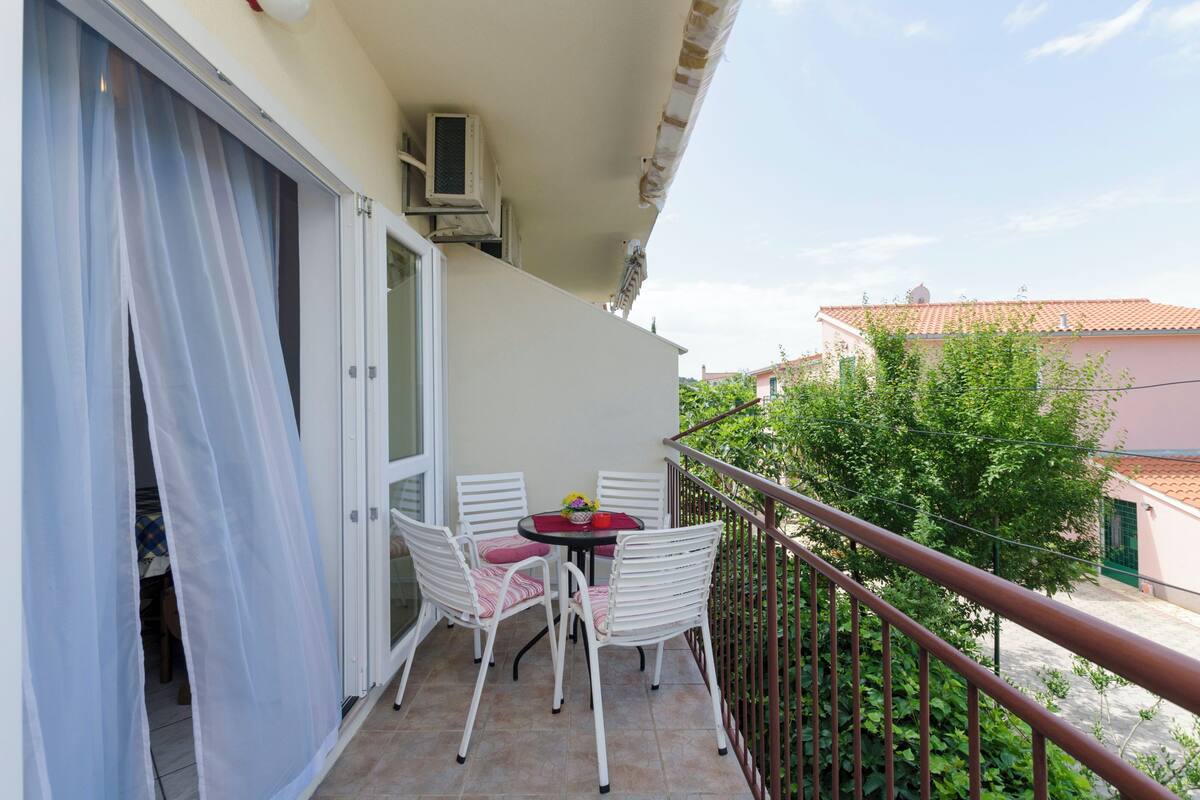 Un balcon avec des chaises blanches, une petite table ronde et un appareil de climatisation blanc.