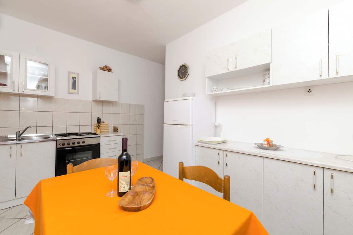 Une cuisine moderne avec des meubles blancs, une cuisinière, un four et une table à manger agrémentée d’une bouteille de vin et d’un verre.