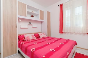 Une chambre à coucher avec un lit, des étagères intégrées, une fenêtre avec des rideaux et un tapis rouge.