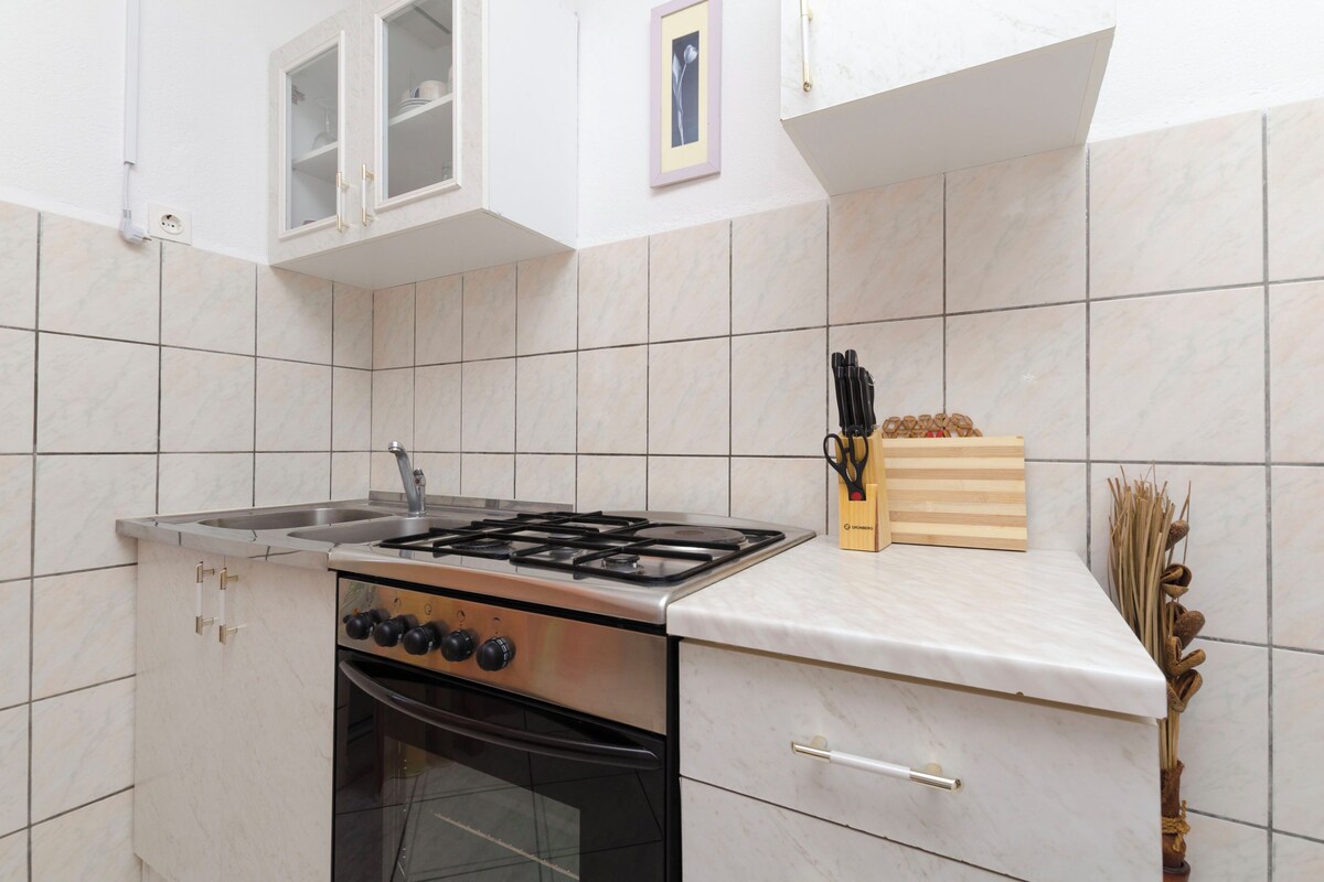 A kitchen with a gas stove, oven, and a sink. There are cabinets, a countertop, and a picture frame on the wall.