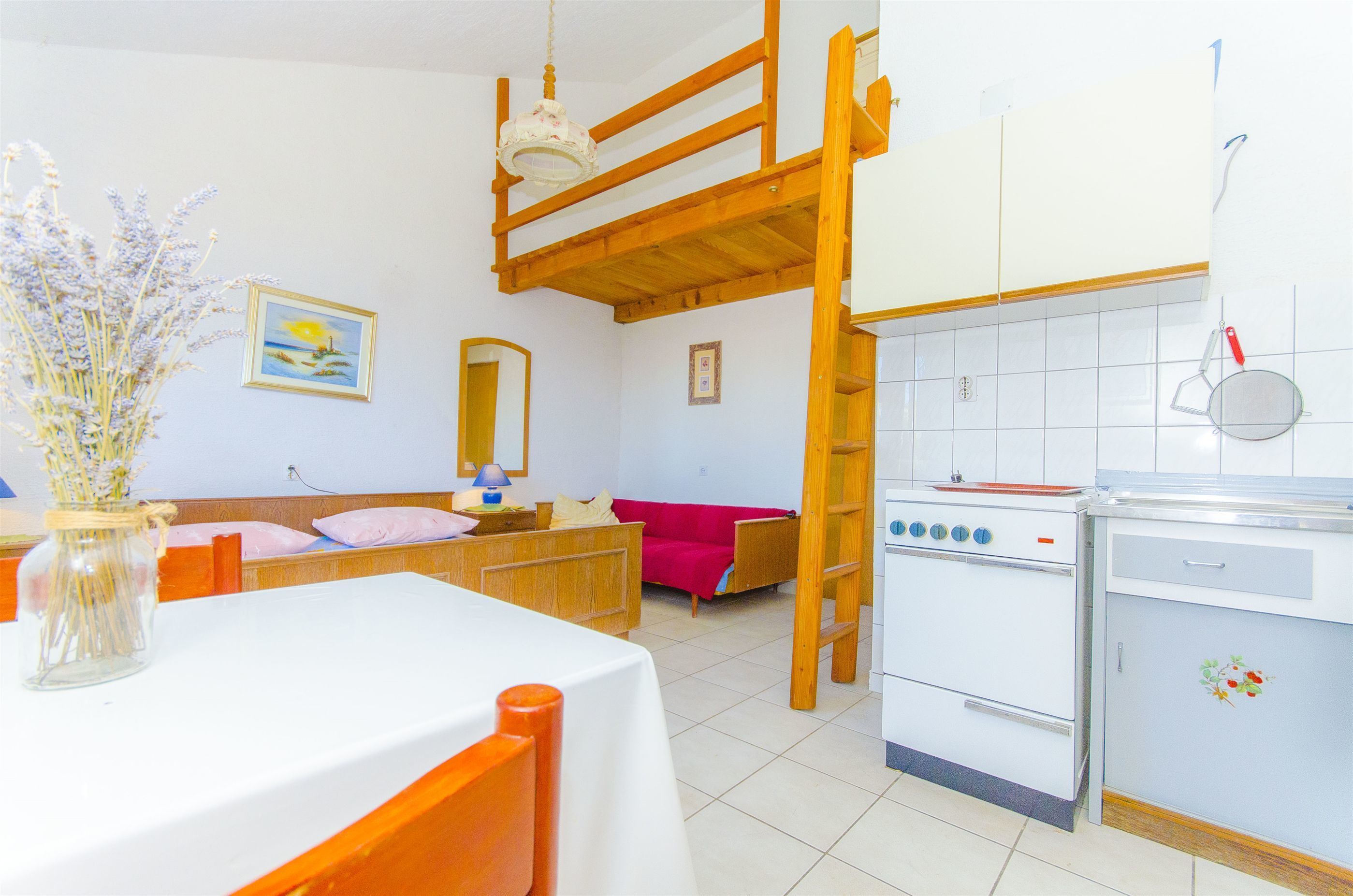 A kitchen with a stove, sink, and wooden ceiling. There is a table with a vase of flowers and a red couch in the background.