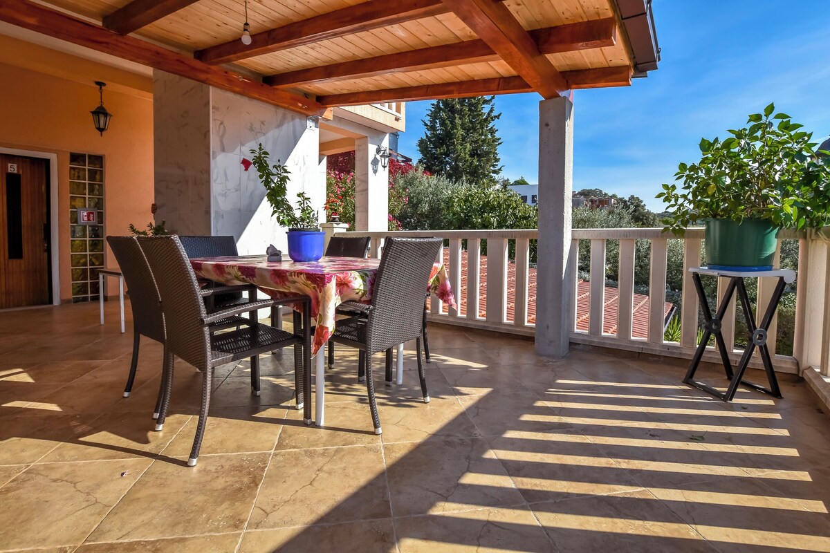 A covered patio with a table and chairs, potted plants, and a view of the surrounding area.