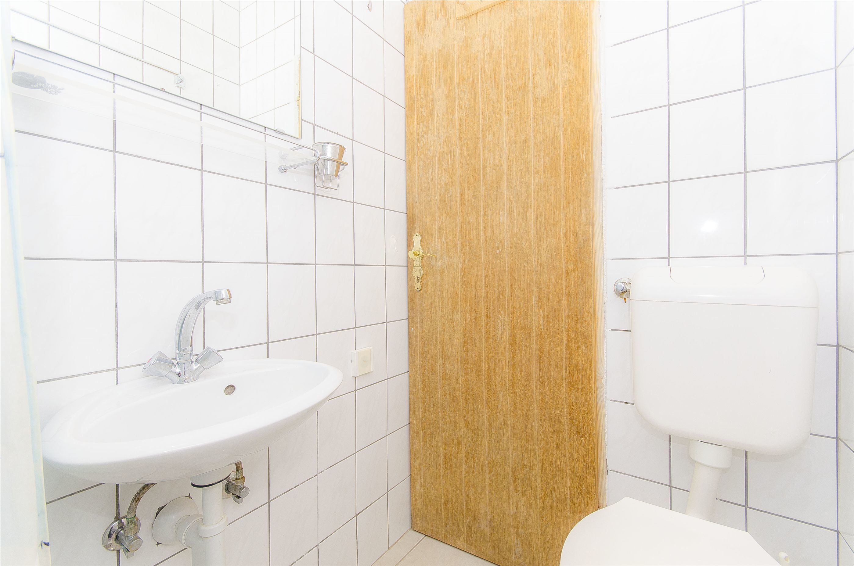 A bathroom with a white sink, a wooden door, and a white toilet.