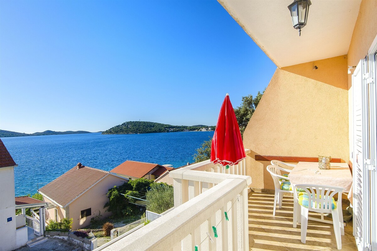 A balcony with a table and chairs, overlooking a body of water and hills.