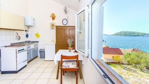 A kitchen with a view of the sea, a dining table, and a wooden chair. - Apartments Pera (Razanj)
