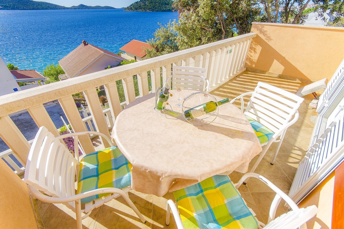 A balcony with a table and chairs, overlooking a body of water and a mountainous landscape.