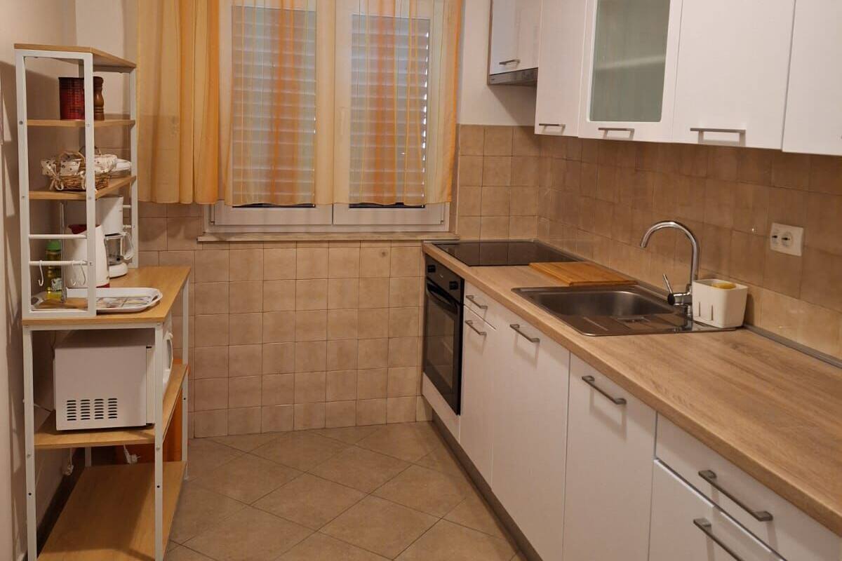 A compact kitchen with white cabinets, a sink, and a window with orange curtains.