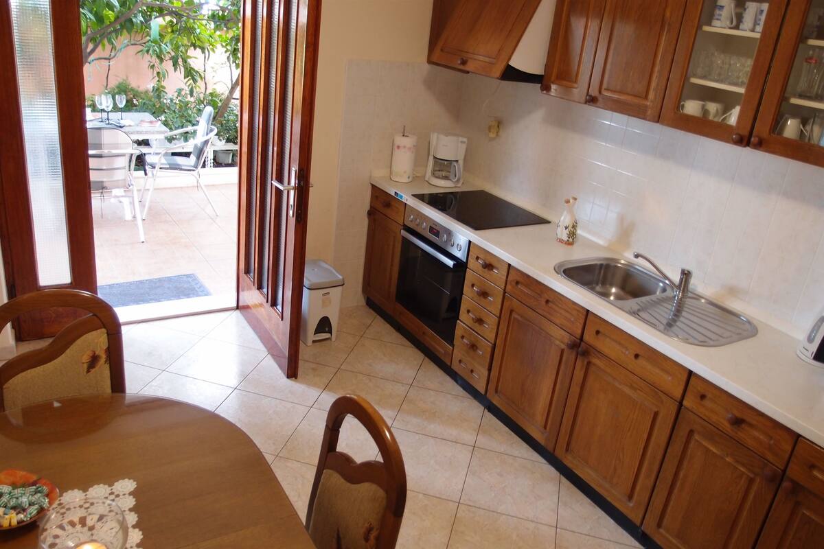 A kitchen with wooden cabinets, a sink, and a stove. There is a dining table with chairs and a small table with a decorative item.