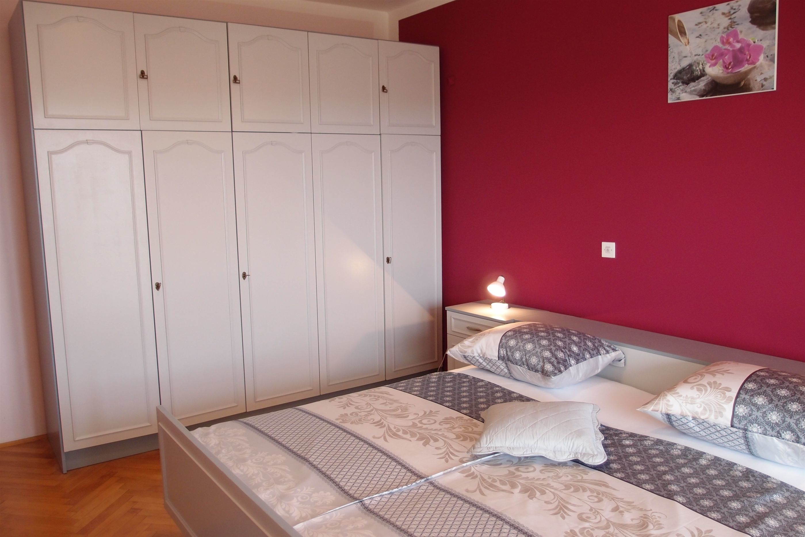 A bedroom with a bed, two bedside tables, a wardrobe, and a wall-mounted picture.