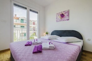 A bedroom with a bed, a window, a balcony, and a flower painting on the wall.