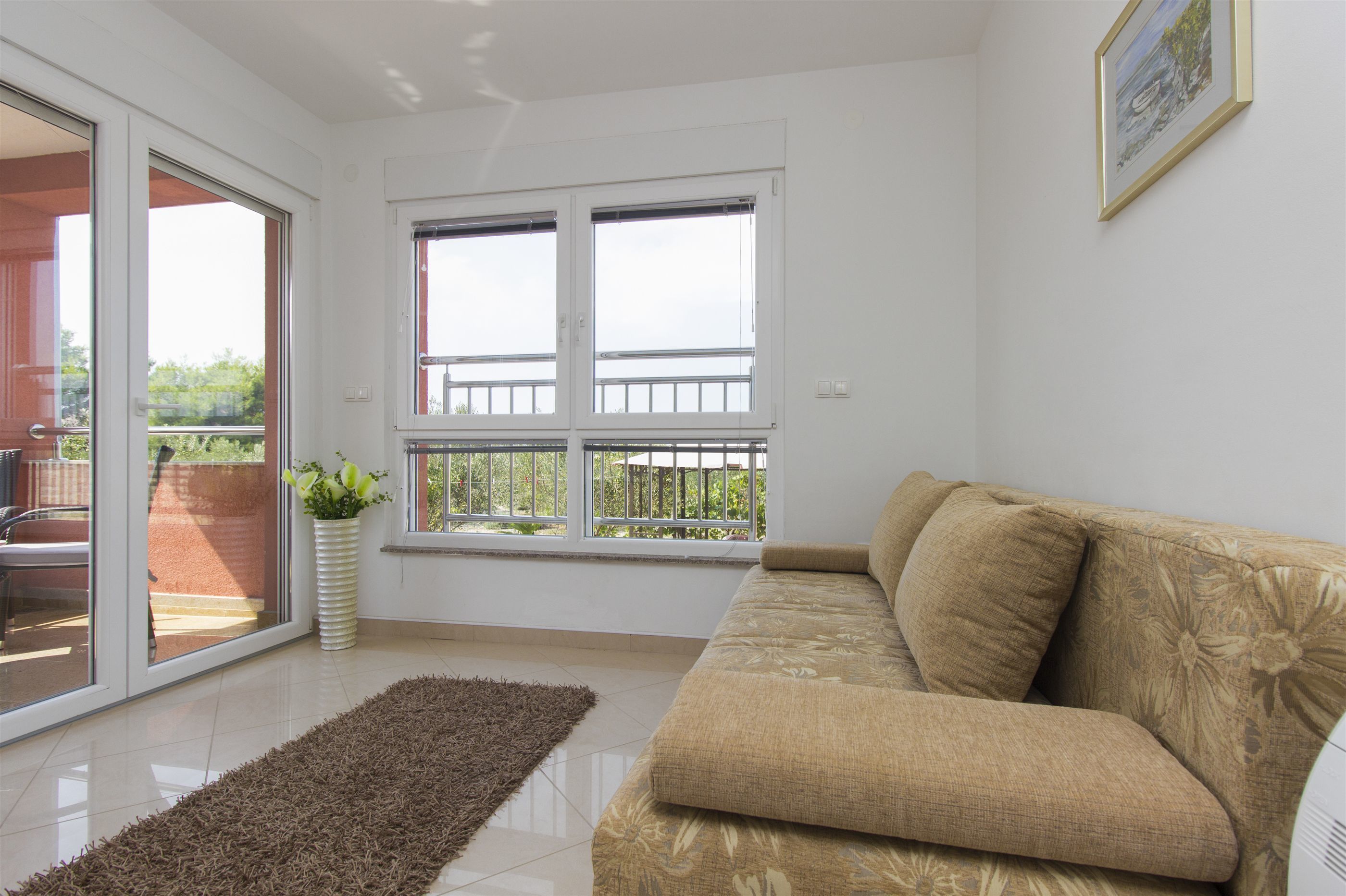 A living room with a beige sofa, a large window with a view of greenery, and a potted plant.