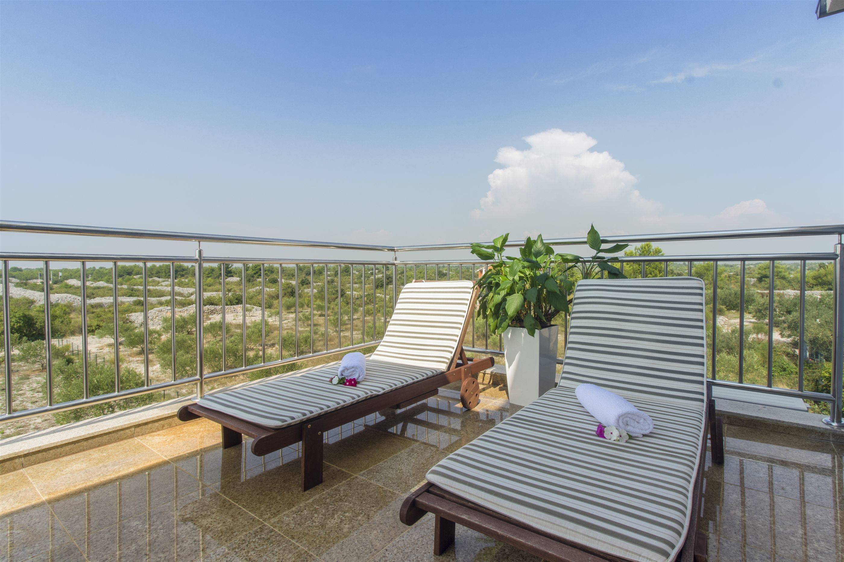 A balcony with two lounge chairs, a potted plant, and a view of a green landscape.