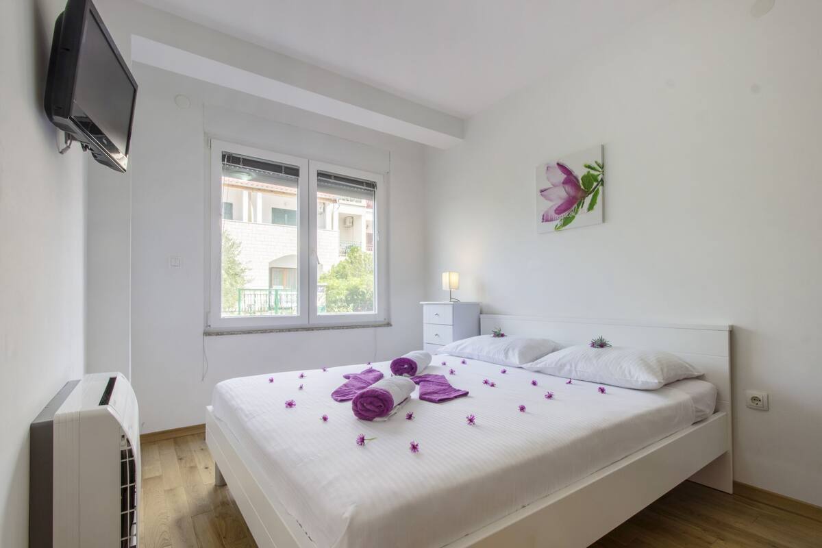 Une chambre d’hôtel avec un lit, un téléviseur fixé au mur, une fenêtre et une table de chevet avec une lampe.