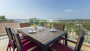Ein Holztisch mit vier weißen Tassen und Untertassen, zwei Karaffen und zwei Gläser Orangensaft auf einem Balkon mit Blick auf eine reizvolle Landschaft.