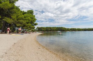 A pebbled beach with clear water, trees, and a partly cloudy sky. - Apartments Lenija (Jadrija)