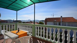 Un balcon agrémenté d’un auvent verdoyant, d’une balustrade blanche et d’une table sur laquelle se trouvent une bouteille et un verre.