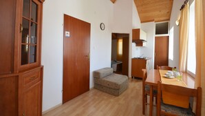 Une pièce de taille modeste, meublée en bois, avec une petite kitchenette et une fenêtre agrémentée de rideaux.