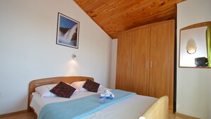 Une chambre avec un plafond en bois, un lit recouvert d’une couverture bleue, une armoire en bois et un tableau encadré accroché au mur.