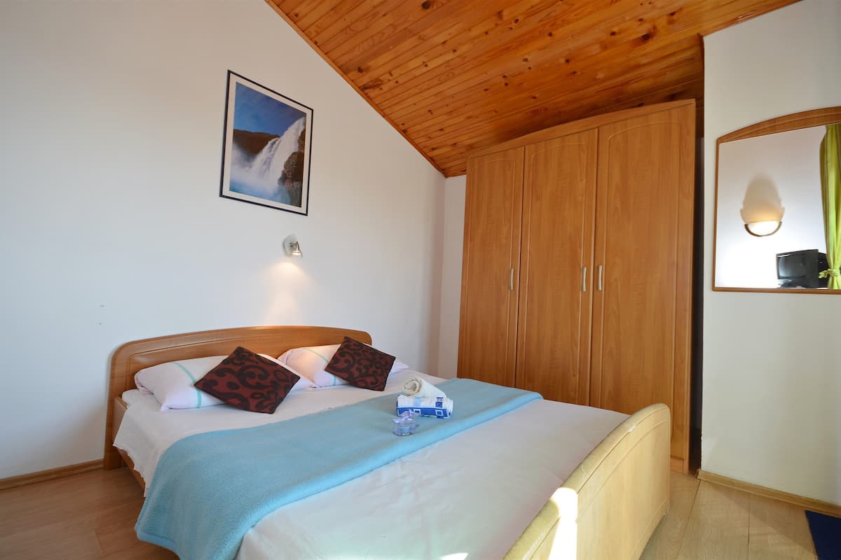 Ein Schlafzimmer mit Holzboden, einem Bett mit blauer Decke, einem Schrank aus Holz und einem gerahmten Bild an der Wand.