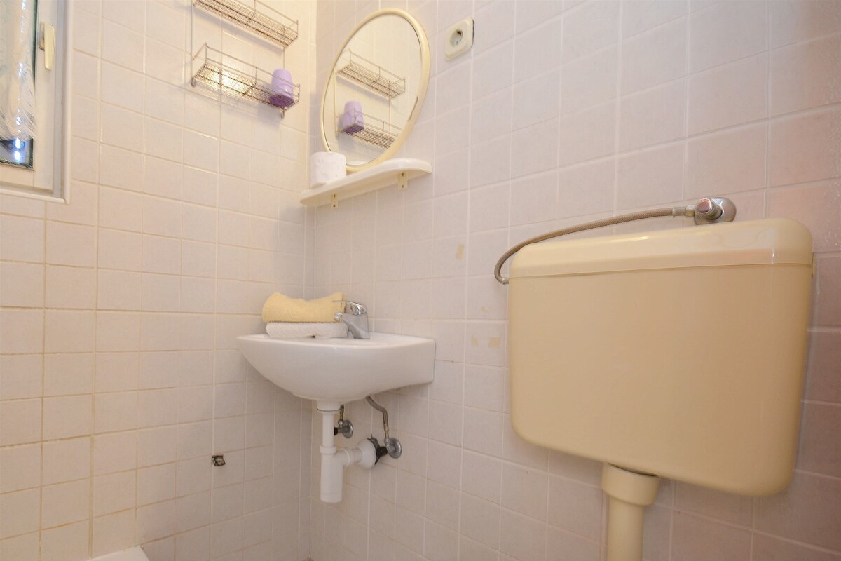 A bathroom with a white sink, mirror, and toilet. There are shelves above the mirror holding toiletries.