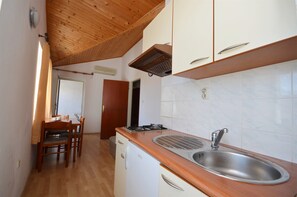 A compact kitchen with wooden cabinets, a stainless steel sink, and a small refrigerator. - Apartments Nada (Vodice)