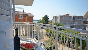 A balcony with a table set for two, featuring a bottle and a plate of watermelon. - Apartments Sime (Srima)