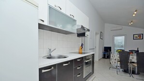 A modern kitchen with a built-in oven, a sink, and a dining area with a table and chairs. - Apartments Sime (Srima)
