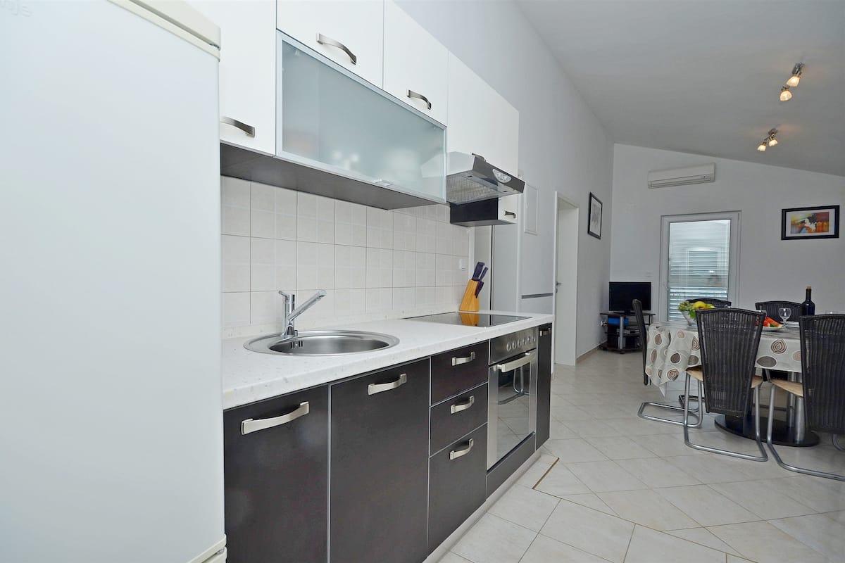 A modern kitchen with a built-in oven, a sink, and a dining area with a table and chairs.
