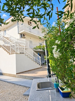 A building with a white exterior, a staircase with white railings, and a potted plant with white flowers. - Apartments Sime (Srima)