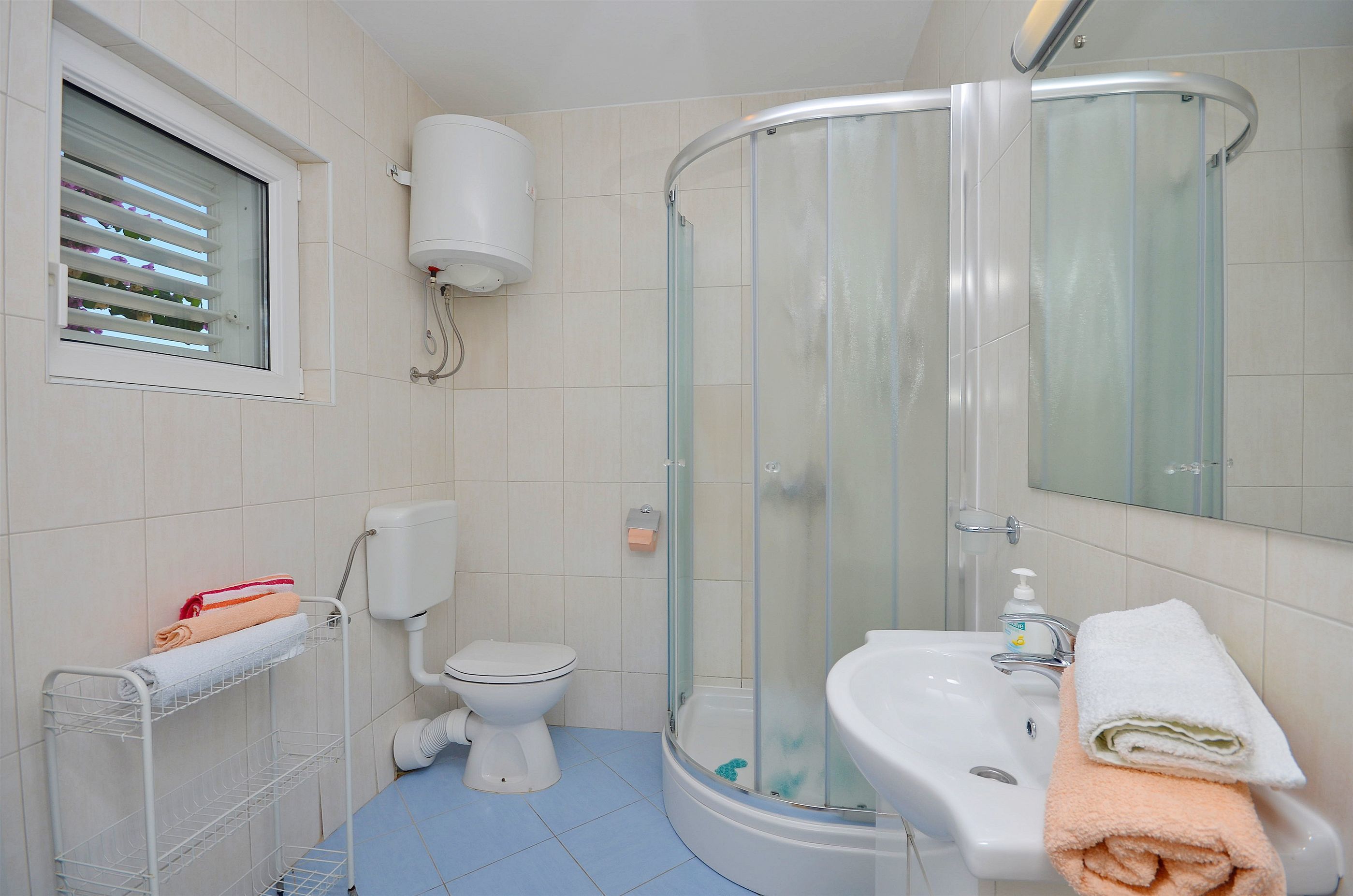 Un bagno con un WC, una cabina doccia in vetro, un lavandino e una finestra con persiane.