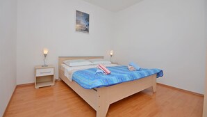 A bedroom with a wooden bed, white walls, a small bedside table, and a nightstand. - Apartments Sime (Srima)