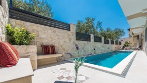 A poolside area with a stone wall, a bench, and a decorative vase. - Apartments Vanja (Novalja)