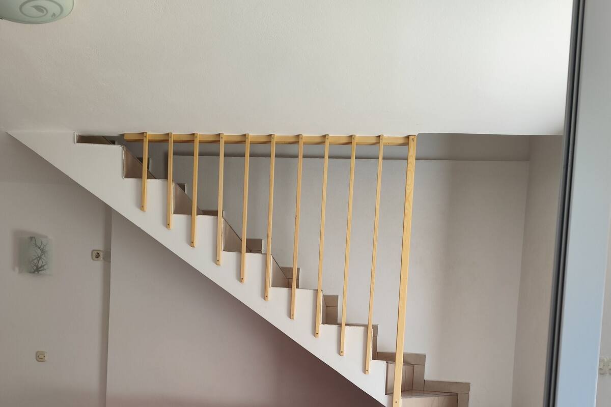 Un escalier avec des rampes en bois, un canapé rouge avec des coussins verts et un sol carrelé.