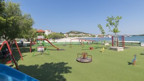 A playground with various play equipment, a slide, and a view of the beach and sea in the background. - Apartments Emil (Murter)