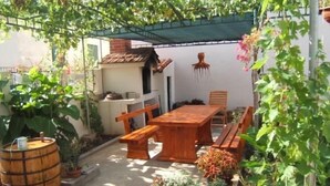A wooden table and benches in a garden area with plants and a barrel. - Apartments Emil (Murter)