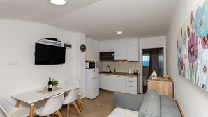 Un espace de vie compact comprenant un coin cuisine, un coin repas avec une table et des chaises, un canapé et un téléviseur fixé au mur.