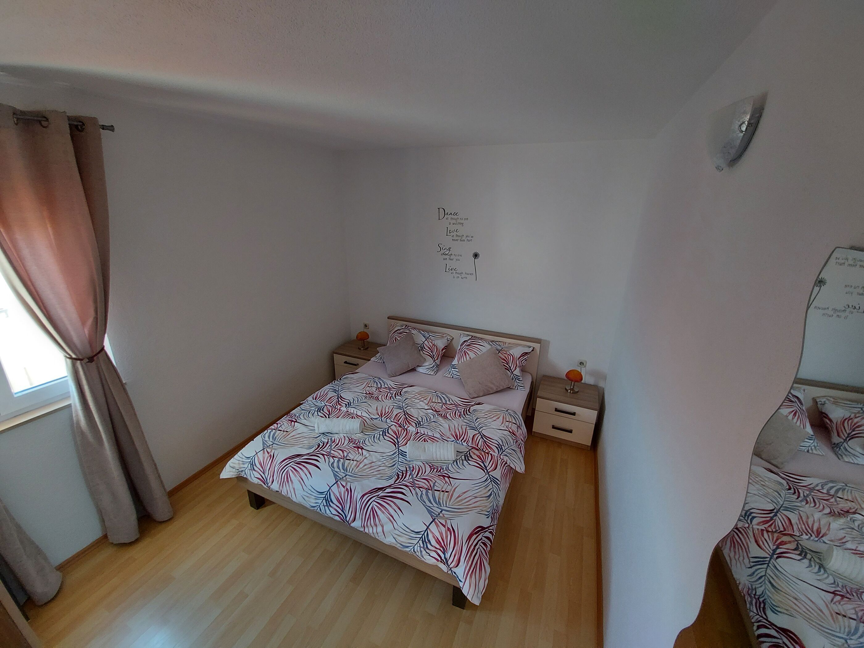 Une petite chambre à coucher, bien rangée, avec un lit simple, une table de chevet, une commode et une étagère fixée au mur.