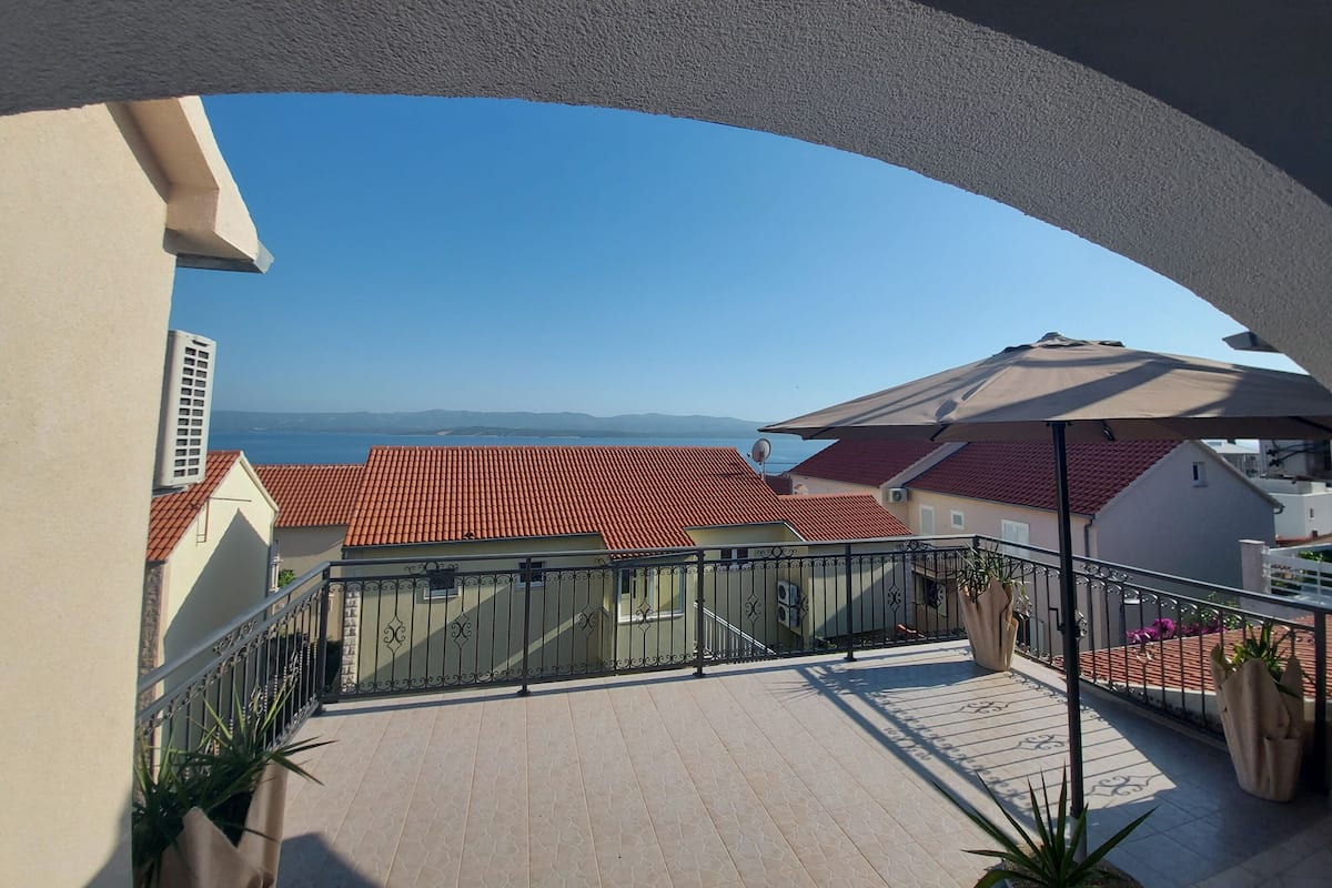 A balcony with a view of the sea and red-roofed buildings.