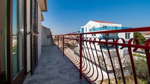 Un balcone con ringhiera in metallo rosso, una porta in vetro e vista su un edificio moderno con tetto blu.