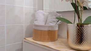 A bathroom with a bamboo basket holding white towels, a decorative plant in a textured vase, and a tiled wall. - Apartments Ivana (Nin)
