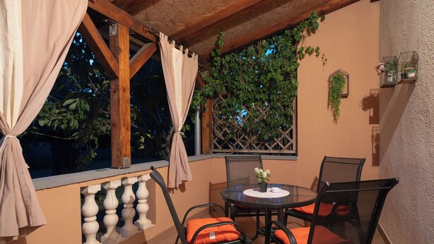 A balcony with a table and chairs, a window with curtains, and a wall-mounted planter with greenery. - Apartments Ivana (Nin)