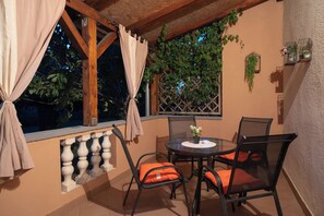 Een balkon met een tafel en stoelen, een raam met gordijnen en een wandplanter met beplanting.