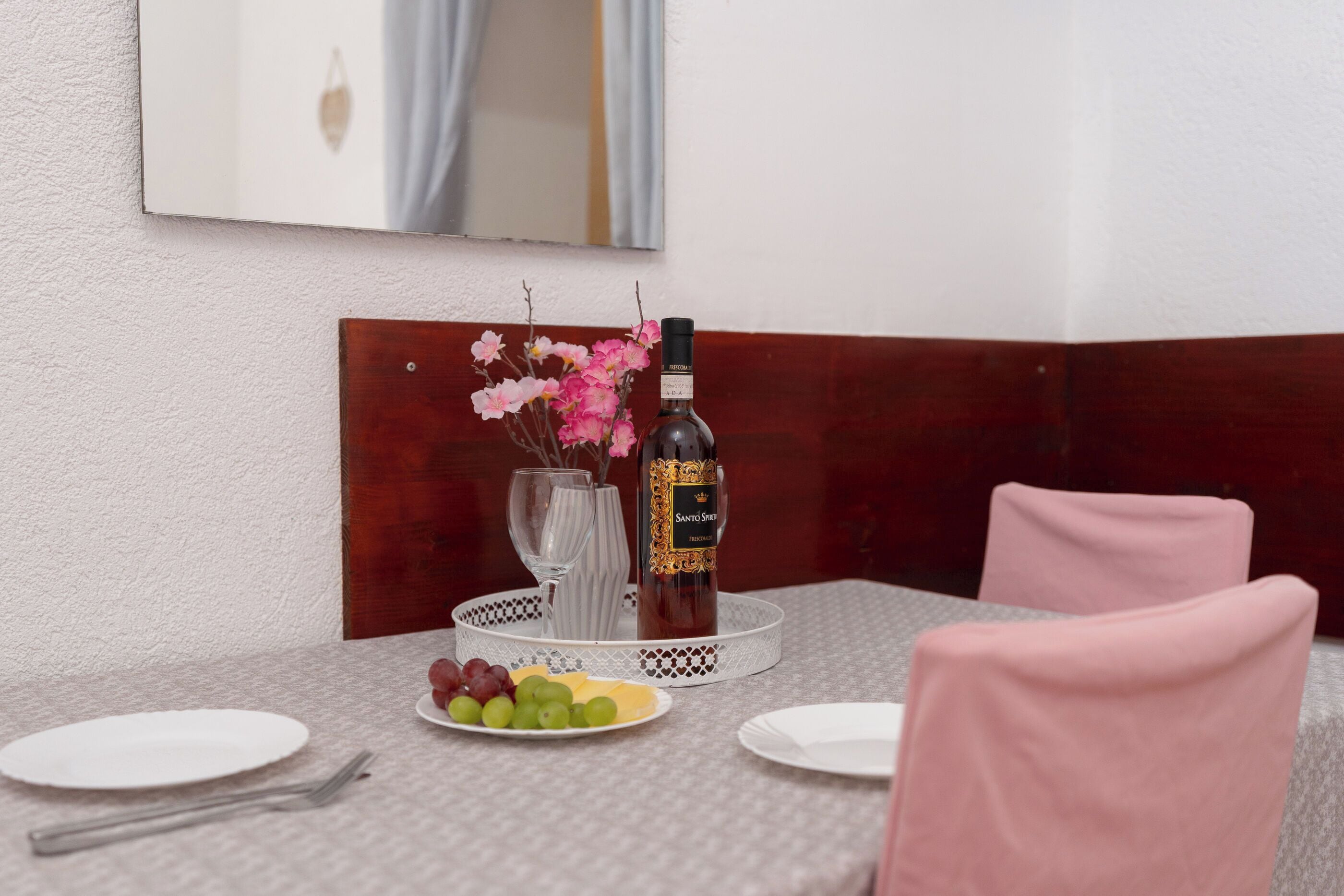 Una mesa de comedor con una botella de vino, un plato de uvas y un florero con flores.