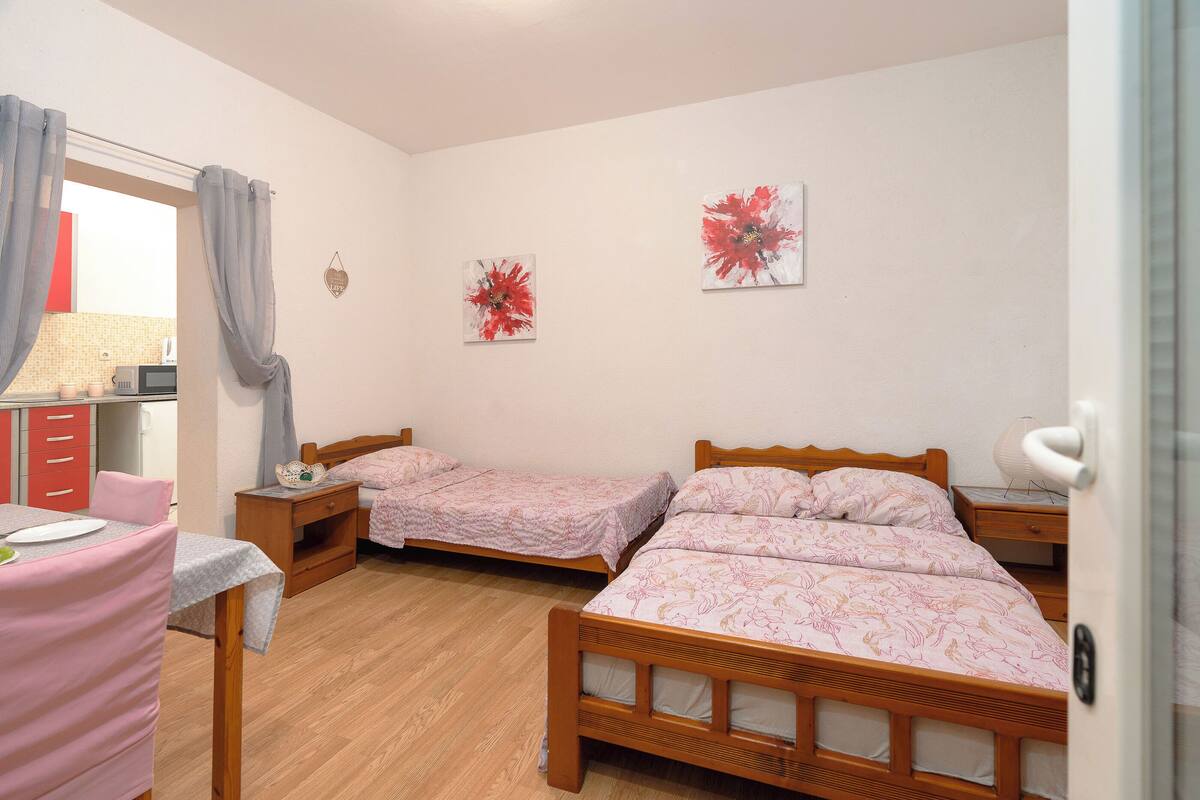 Camera da letto con due letti singoli, un comò in legno, un tavolo con una sedia e due quadri appesi al muro.