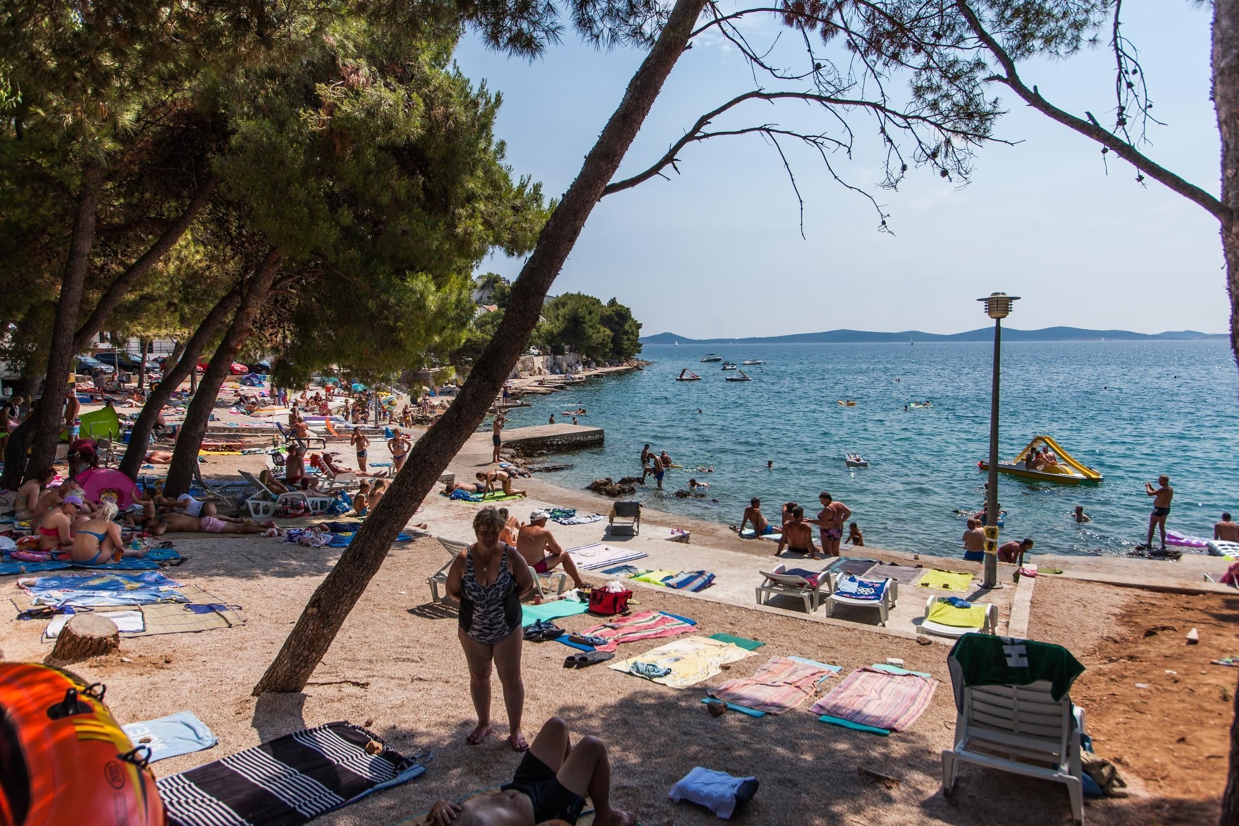 A beach scene with people sunbathing, swimming, and boats on the water.