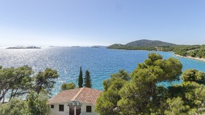 A coastal view with a clear blue sea, green hills, and a building with a tiled roof. - Apartments Vlasta (Tribunj)