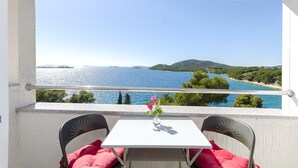 A balcony with a white table and two chairs, overlooking a coastal view with trees and a body of water. - Apartments Vlasta (Tribunj)